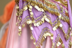 Partial view of woman's pink silky skirt with gold beading hanging from the tiers