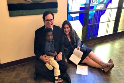 Smiling white couple and their Black son sitting in a synagogue with stained glass behind them
