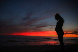 Silhouette of a pregnant person against a brightly colored sunset 