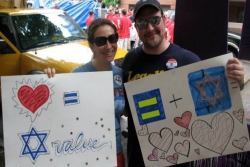 Two smiling people holding Jewishly themed Pride Parade signs