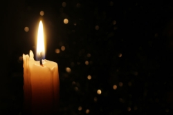 Single lit candle against a dark background with light shimmer effect