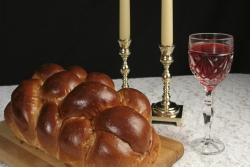 challah on a cutting board, candles and wine, all on a table covered by a white lace tablecloth