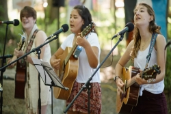 Three young people playing guitars at a summer camp worship service