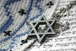 Star of David necklace lying on an open Torah and yarmulke
