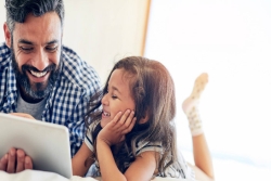 Dad and daughter laughing together as they look at a tablet screen