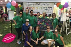 Group of people wearing synagogue shirts and standing in front of a rainbow welcome banner