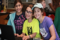 Three young girls in bright summer tees around a computer