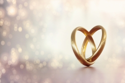 Two gold wedding bands entwined together to form the outline of a heart; glittery lights in the background