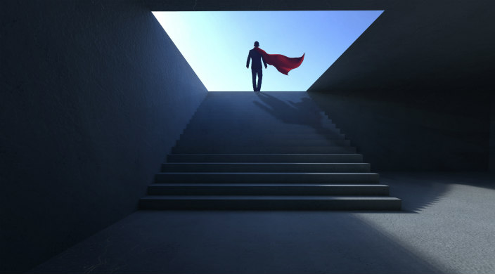 Shadowy profile of a man in a superhero cape walking up a flight up stairs 
