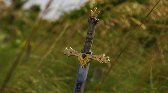 Silver sword encrusted with jewels stuck into the side of a grassy hill