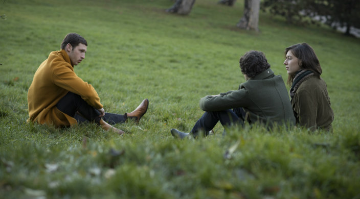 Scene from the movie: three actors (two men and one woman) sitting in a grassy field