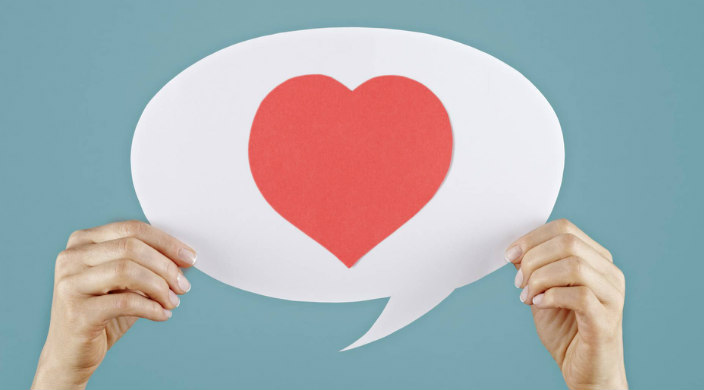 Hands holding up a white cutout of a speech bubble with a heart on it 