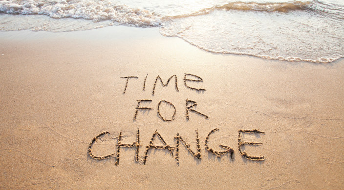 Time for change written in the sand with waves coming toward the words