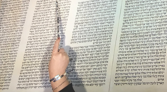 Hand holding yad and marking place in Torah scroll