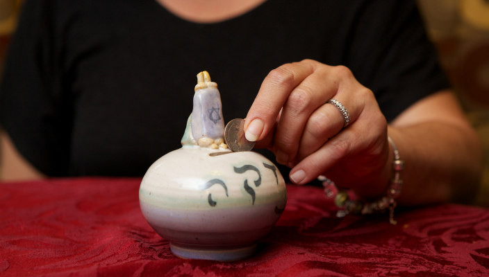 Hand dropping a coin into a ceramic tzedakah box