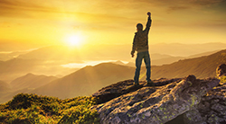 A hiker at sunrise raises his fist in victory
