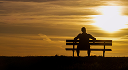 A man on a bench contemplates the sunset