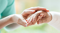 A woman holds a senior's hand