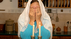 A woman covers her face with her hands to recite the Shabbat blessing over candles