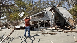 a distraught man looks at his house that was destroyed in a hurricane