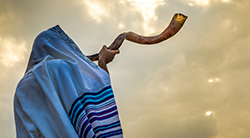a man wearing a talit blows a shofar