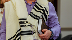 a man wears a tallit and carries a siddur