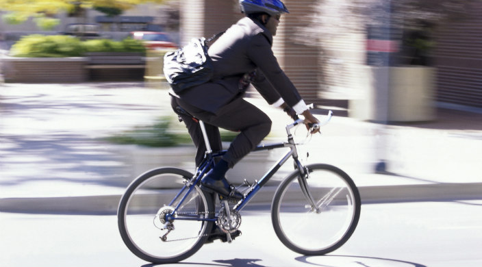 man in suit and bike helmet riding a two-wheeled bike on an urban street