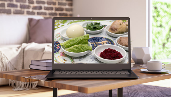 Laptop set up in a home living room with a seder plate displayed on the screen screen