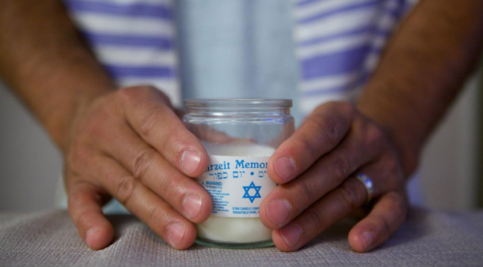 Hands of a person who is wearing a tallit (prayer shawl) holding a yahrzeit candle