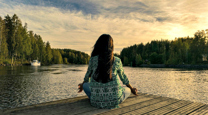 Woman in a yoga pose on a dock facing nature